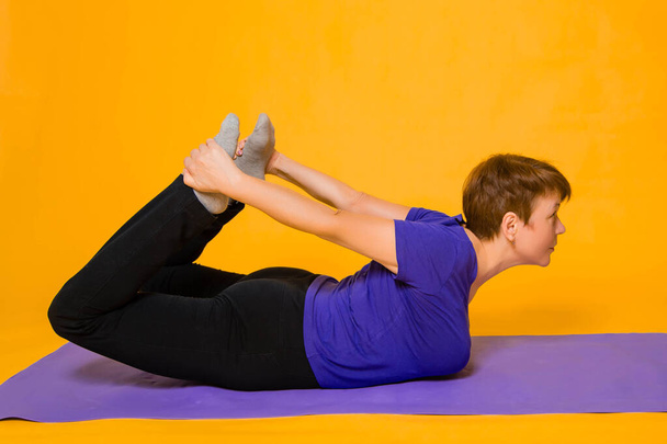 Aged woman doing yoga on a purple rug. Studio photo on a yellow background. - Foto, immagini
