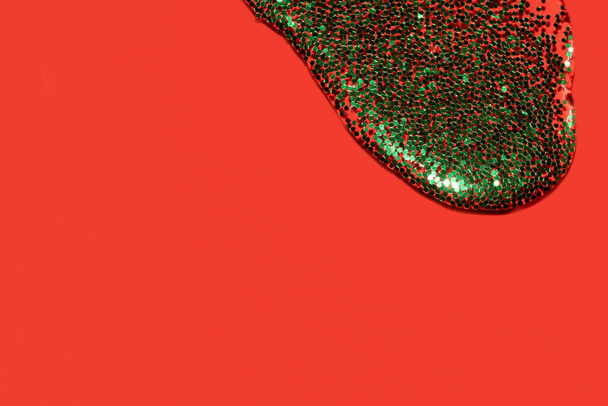líquido transparente con purpurina verde vertiendo sobre un fondo rojo coral - Foto, imagen