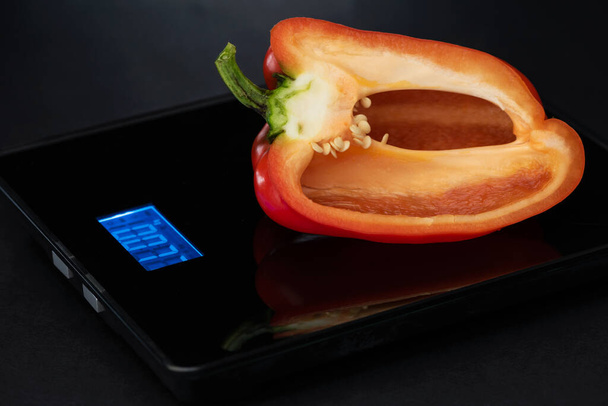 Il taglio in metà di pepe rosso è su un peso elettronico su uno sfondo nero. - Foto, immagini
