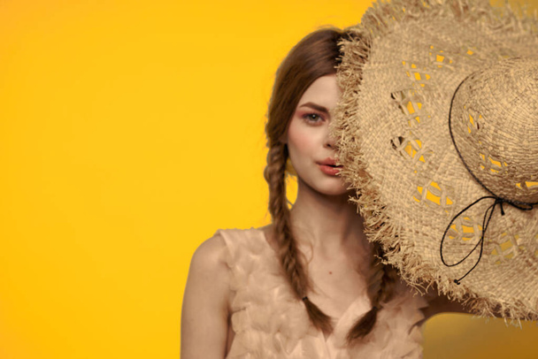 Nő egy szalma kalap a kezében egy sárga háttér érzelmek vágott nézet  - Fotó, kép