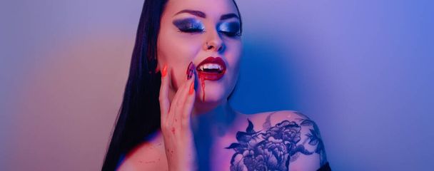 Mujer vampiro, morena con labios rojos y sangre de la boca, colmillos. Tatuaje en todo el hombro, neón traje de halloween - Foto, imagen