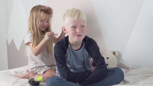 Zabawna młodsza siostra robi zabawną fryzurę starszemu bratu - Materiał filmowy, wideo