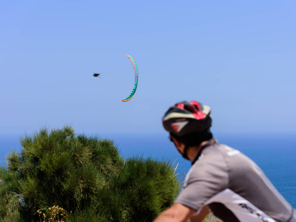 Cyclist looking on Flying tandem paragliders in the sky over the sea, unfocused beautiful sea view - Photo, Image