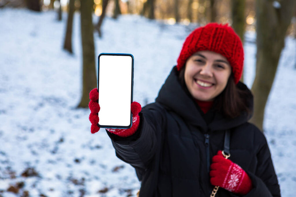 giovane donna sorridente in abito invernale in possesso di telefono con bianco spazio vuoto copia schermo - Foto, immagini