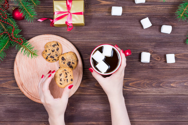 Female hands with a cup of tea and cookies on a wooden table with a christmas tree and decorations - Фото, зображення