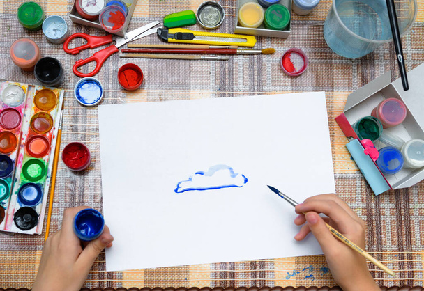 egy lány akvarell kék felhőket rajzol egy üres fehér papírra, művészi alkotás otthon, kreatív alkotásokat készít - Fotó, kép