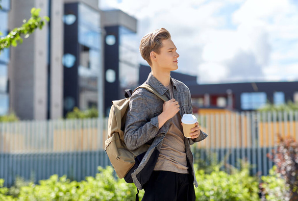 young man with backpack drinking coffee in city - Photo, image