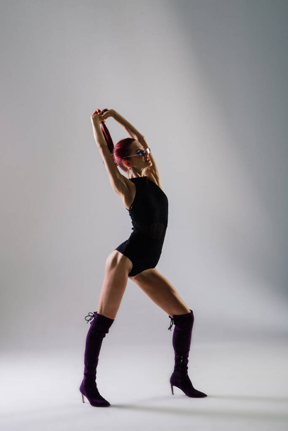 Jovem bela fêmea flexível em um macacão preto e salto alto está posando em um estúdio de dança. - Foto, Imagem