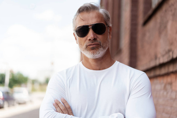 Portrait of a Grey-haired Mature handsome man in jeans and white t-shirt leaning to the old wall - Foto, immagini