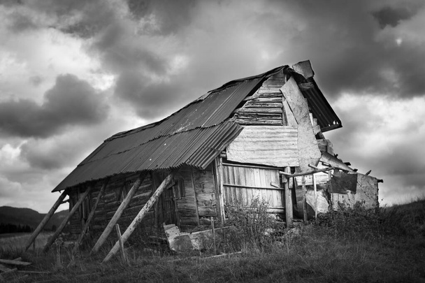 Bianco e nero di una vecchia e fatiscente baracca in legno e metallo sulle montagne dell'altopiano di Asiago. Cielo tempestoso. Enego, Vicenza, Italia - Foto, immagini