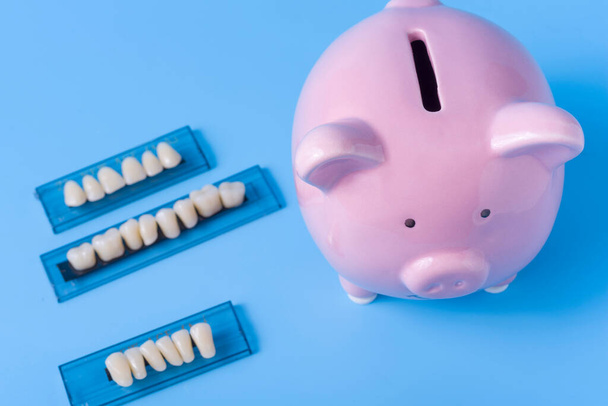 Piggy Bank op een blauwe achtergrond en tandheelkundige instrumenten. Het concept van het besparen van geld voor de vervaardiging van tandheelkundige implantaten en behandeling. - Foto, afbeelding