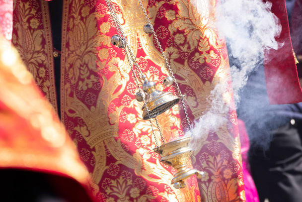 Un incensario fumador en la mano de un sacerdote cristiano ortodoxo en una sotana de iglesia bordada. - Foto, Imagen