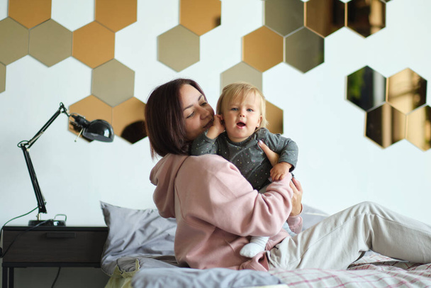 幸せな家族の母親と赤ちゃんの遊びベッドで抱き合って笑って - 写真・画像