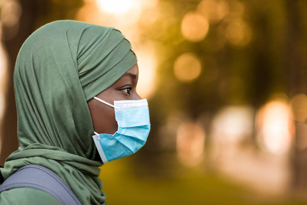 Profil der schwarzen muslimischen Frau mit medizinischer Maske und Hijab im Freien - Foto, Bild