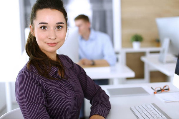 Business woman using computer at workplace in modern office. Brunette secretary or female lawyer looking at the camera and happy smiling. Working for pleasure and success - Photo, Image