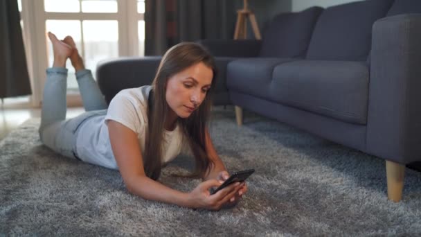 Egy nő fekszik a padlón és okostelefont használ.. - Felvétel, videó