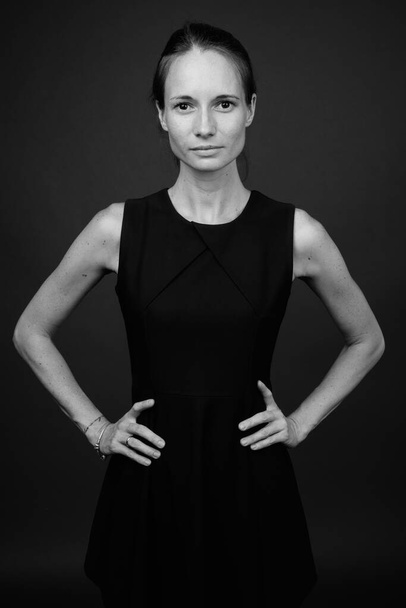Studio shot of beautiful woman wearing black sleeveless dress against gray background - Φωτογραφία, εικόνα