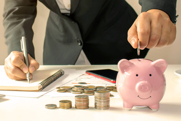 Nahaufnahme einer Geschäftsfrau, die eine Münze in einem Sparschwein hält, ein Konzept, um Geld für die Finanzbuchhaltung zu sparen. - Foto, Bild