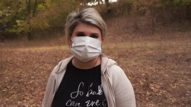 Jonge vrouw draagt een beschermend masker buiten. Zet masker op tijdens het wandelen in een park als gevolg van covid-19 pandemie - Video