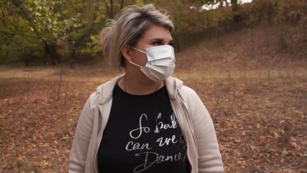 Mujer joven lleva una máscara protectora al aire libre. Póngase una máscara mientras camina en un parque debido a la pandemia de covid-19 - Imágenes, Vídeo