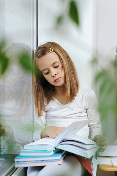 La chica está sentada en el alféizar de la ventana leyendo un libro. - Foto, Imagen