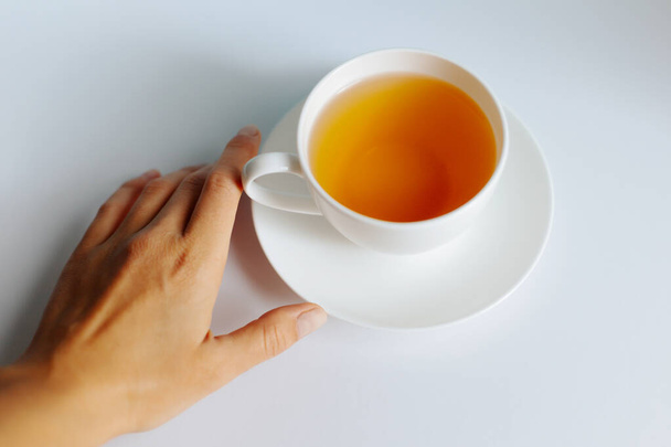 Bir kadın eli beyaz masada bir fincan çay tutar. Beyaz arka planda yeşil çay. - Fotoğraf, Görsel
