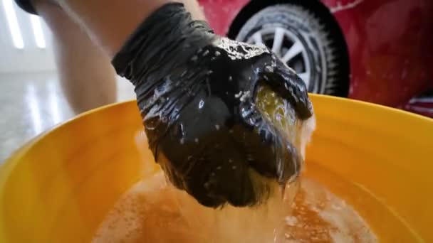 Człowiek pracownik myje czerwony samochód na myjni samochodowej z żółtą ścierką. - Materiał filmowy, wideo