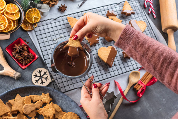 woman glazing Christmas biscuits with liquid chocolate on a kitchen table - Photo, image