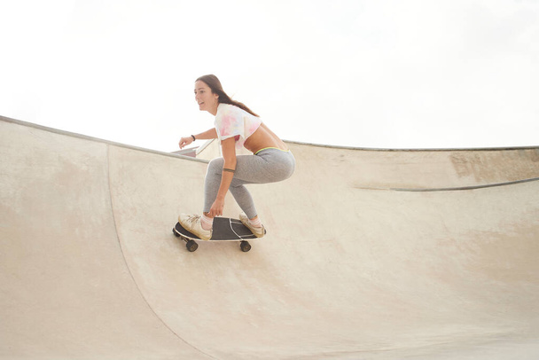 Meisje rijdt op een skateboard in de kom van een skatepark. Grijze achtergrond. - Foto, afbeelding