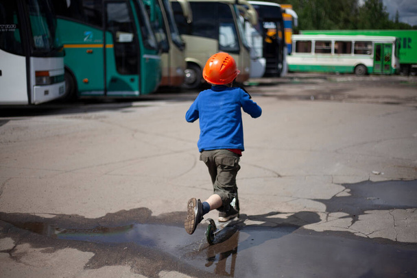 A child on a scooter on the street. A boy in an orange helmet rides a scooter.  - Zdjęcie, obraz