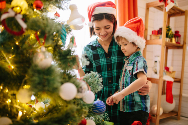 Happy family mom and son on a Christmas winter sunny morning in a decorated Christmas celebration room with a Xmas tree and gifts - 写真・画像