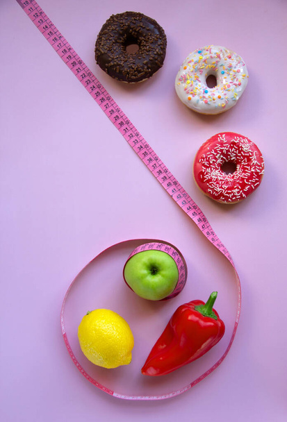 Trendikäs ulkoasu tuoreita hedelmiä, vihanneksia ja donitseja mittausteipillä vaaleanpunaisella taustalla. Ajoittainen, keto, detox ja hoikka ruokavalio. Terveellisen ravitsemuksen käsite. Tasainen lay, kopioi tilaa. - Valokuva, kuva