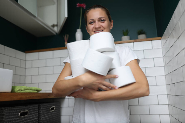 Femme se tient dans les toilettes et tient pile de rouleaux de papier toilette dans ses mains. - Photo, image