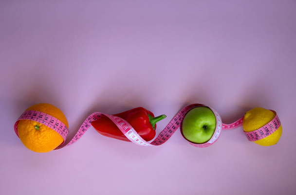 Trendiges Layout mit frischem Obst und Gemüse mit Maßband auf rosa Hintergrund. Intermittierende, keto, Detox und schlanke Diäten. Gesunde Ernährung. Flache Lage, Kopierraum. - Foto, Bild