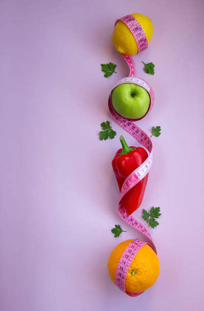 Creative flat lay composition with apple, pepper, lemon, orange with measuring tape on pink background. Intermittent, keto, detox, and slim diets. Healthy nutrition concept. Copy space. - Photo, Image