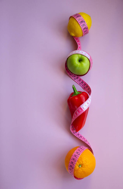 Composição de colocação plana criativa com maçã, pimenta, limão, laranja com fita métrica no fundo rosa. Dietas intermitentes, keto, desintoxicação e magras. Conceito de nutrição saudável. Espaço de cópia. - Foto, Imagem