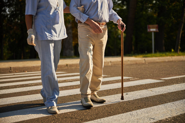 Old man with medicine worker walking on the pedestrian cross in the city - Foto, imagen