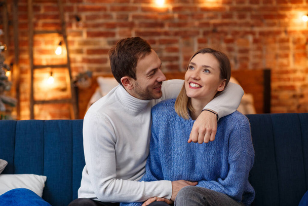 Portrait of beautiful smiling couple hugging at Christmas eve. Beautiful young couple at home enjoying spending time together. Winter holidays, Christmas celebrations, New Year concept - Φωτογραφία, εικόνα