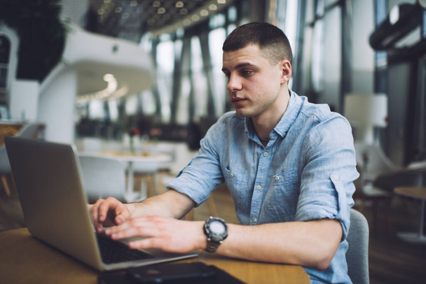 Concentrated male in casual clothes sitting at table in modern cafe and browsing laptop while working on business project remotely - Foto, Imagem