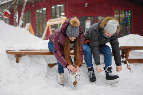 Junge Kerle und Mädchen schnüren Schlittschuhe auf einer Bank in der Nähe der Eisbahn in einem Winterpark. - Foto, Bild