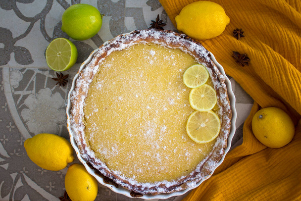 Torta de limão foto vista superior. Torta fresca decorada com fatias de limão e hortelã. Mesa de cozinha cinza azulejos, textura de tecido amarelo, frutas frescas close-up. - Foto, Imagem