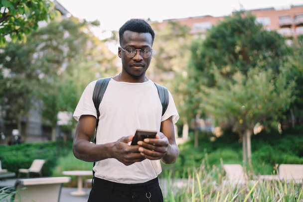 Serious african american hipster guy checking banking account on mobile phone spending free time in city, pensive dark skinned male downloading app on smartphone using 4G connection outdoors - Fotó, kép