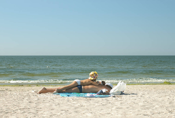Kleines Mädchen sonnt sich auf dem Rücken ihres Vaters an einem sonnigen Strand mit selektivem Fokus und Kopierraum - Foto, Bild