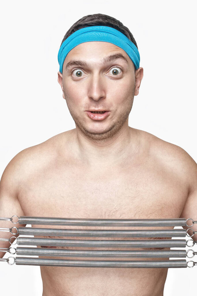 Lustiger Typ mit blauem Schweißband beim Ziehen von Spiralfedern Expander isoliert auf weiß  - Foto, Bild