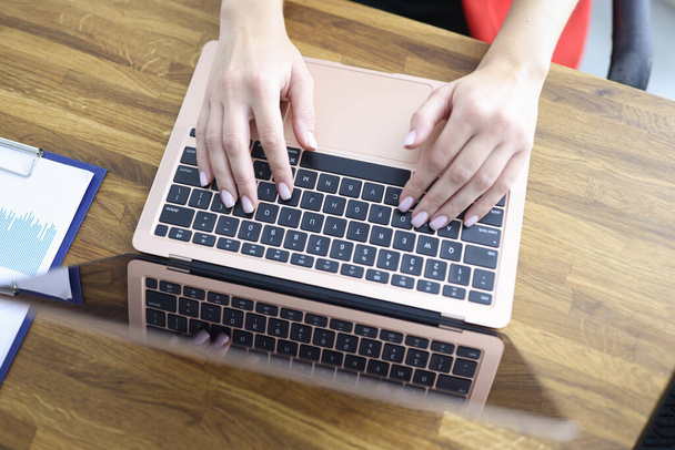 Female hands are typing on laptop keyboard at table in office closeup - Фото, изображение