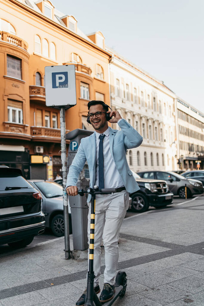 Young modern man using and driving electric scooter on city street and listens to music. Modern and ecological transportation concept. - Fotografie, Obrázek