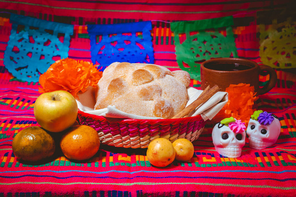 Ημέρα του νεκρού ψωμιού συνοδεύεται με ένα φλιτζάνι καφέ και λευκά κρανία σοκολάτας με ένα παραδοσιακό πολύχρωμο φόντο της ημέρας των νεκρών - Φωτογραφία, εικόνα