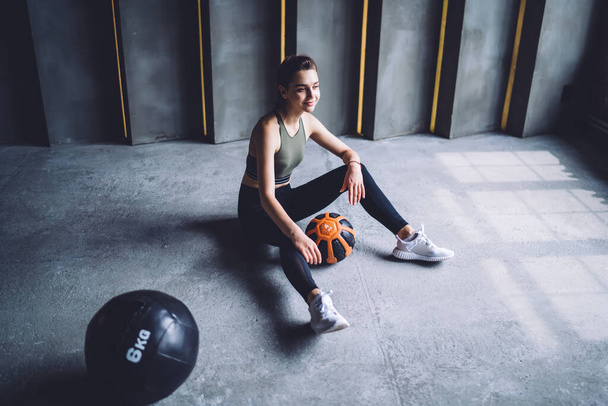 Positive caucasian female in activewear resting after workout in gym dreaming for reaching fitness goals, smiling woman in activewear having break after training for slimming and losing weight - Zdjęcie, obraz