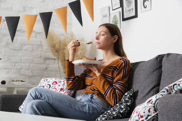 Woman sitting in living room and eating roasted pumpkin slices on plate - Foto, Bild