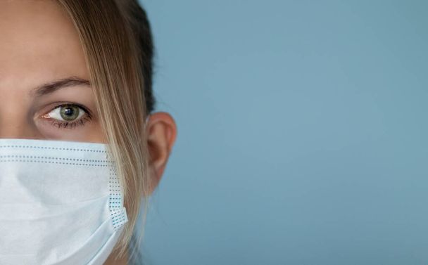 Retrato de una joven con máscara médica, sobre un fondo azul - Foto, Imagen